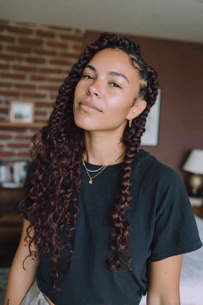 Black boho knotless braids with deep burgundy peekaboo sections and soft wine-red curly tendrils.