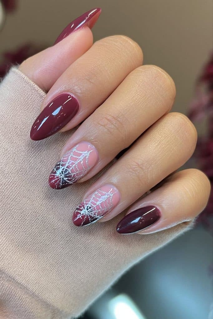 Burgundy spider web nails with rich wine-red polish, glossy black accents, and fine silver webs