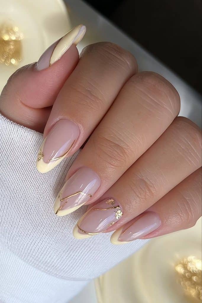 Butter yellow nails with delicate gold foil flecks, fine metallic lines, and elegant accents
