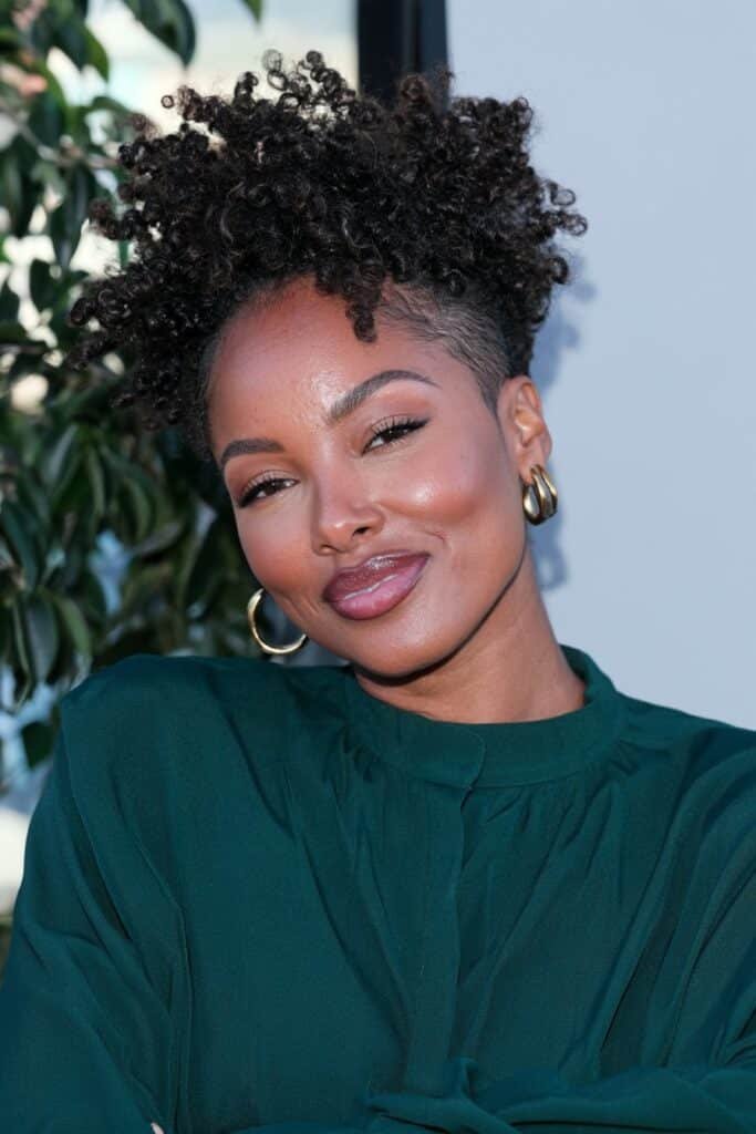Black woman with a curly frohawk hairstyle, featuring defined natural curls down the center and closely tapered sides.