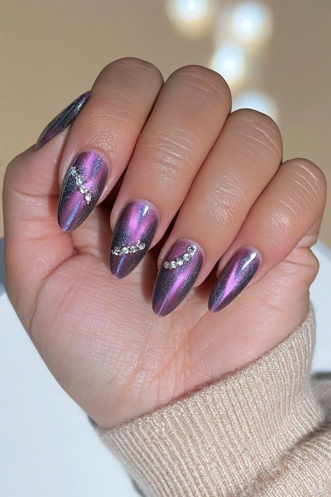 Dark purple cat-eye nails with luminous amethyst streaks and delicate clear rhinestone accents