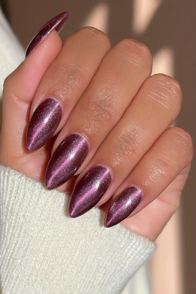 Deep plum cat-eye almond nails with luminous violet ribbons and a glossy finish
