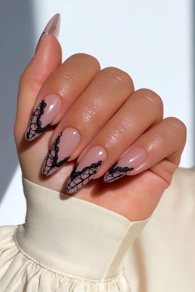 Delicate lace spider web nails with intricate black patterns over a sheer blush-beige base
