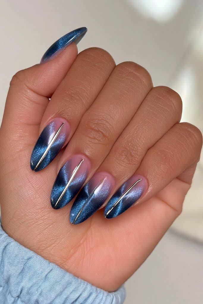 Denim blue cat-eye nails with luminous blue highlights and fine metallic silver stripes