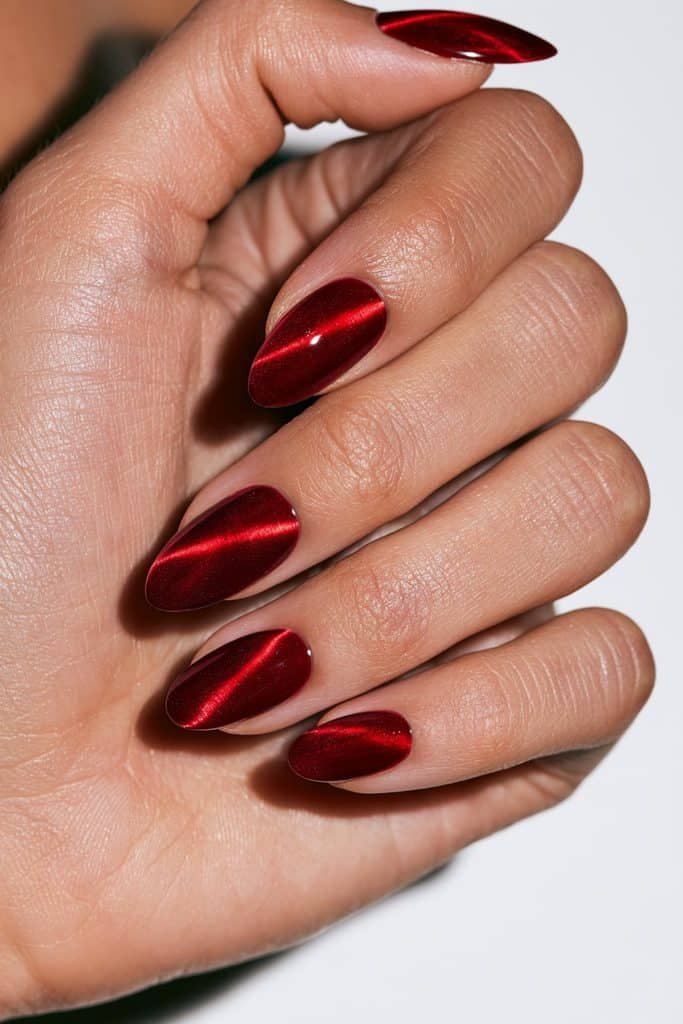 Diagonal red cat eye nails with sharp ruby magnetic stripes sweeping across glossy almond-shaped nails.