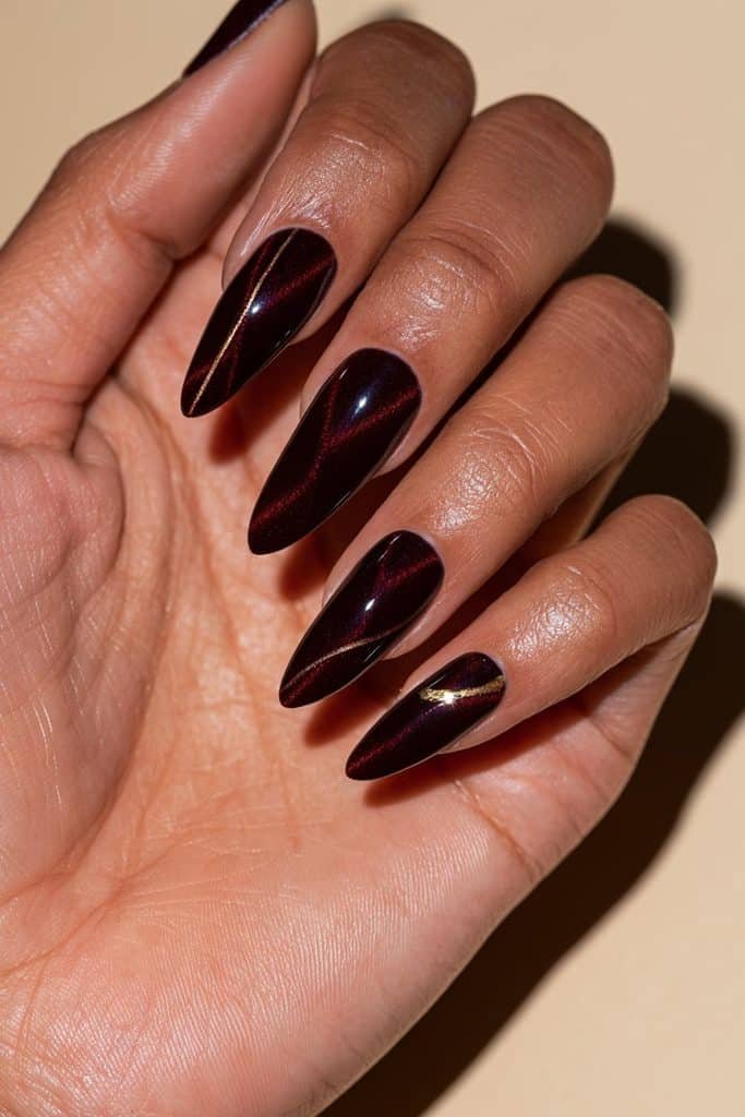 Maroon cat eye nails with delicate gold line accents, subtle gold foil details, and luminous burgundy magnetic polish.