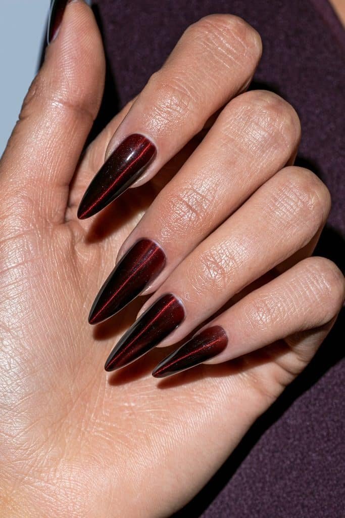 Maroon cat eye jelly nails with translucent black-cherry layers, glowing ruby streaks, and a glossy glass-like finish.