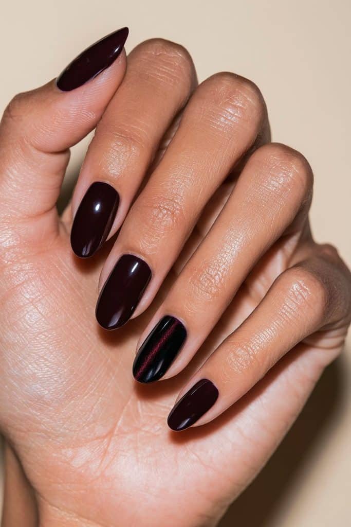 Maroon manicure with four solid burgundy nails and one ruby-shimmer cat eye accent nail on the ring finger.