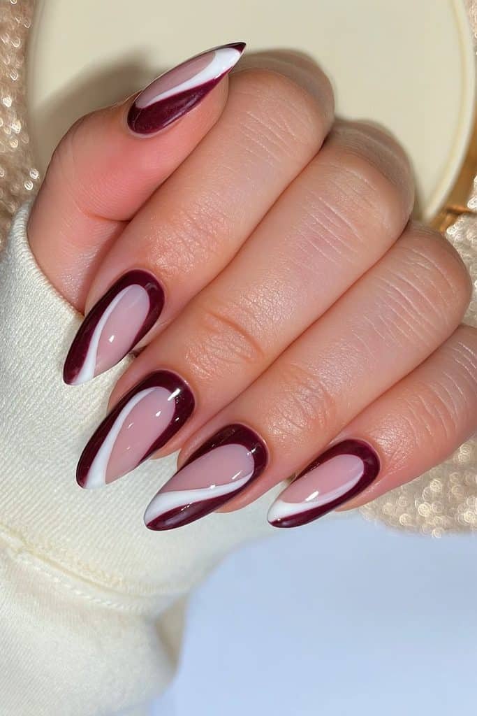Minimalist burgundy nails with curved wine-red sections and clean negative-space details