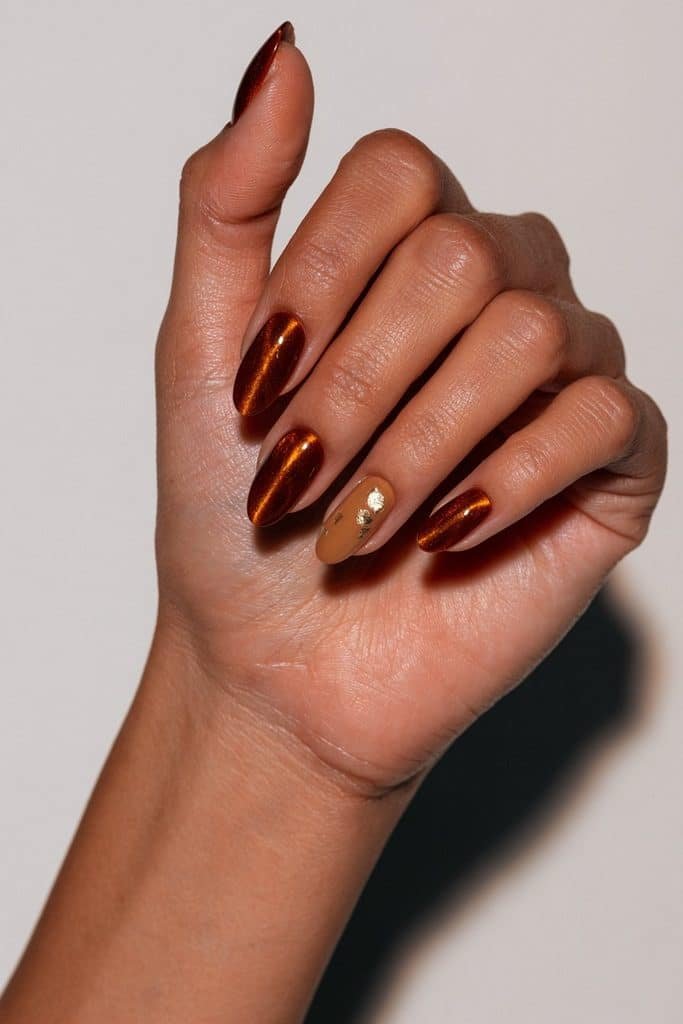 Orange cat eye nails with a contrasting gold foil accent on the ring finger.