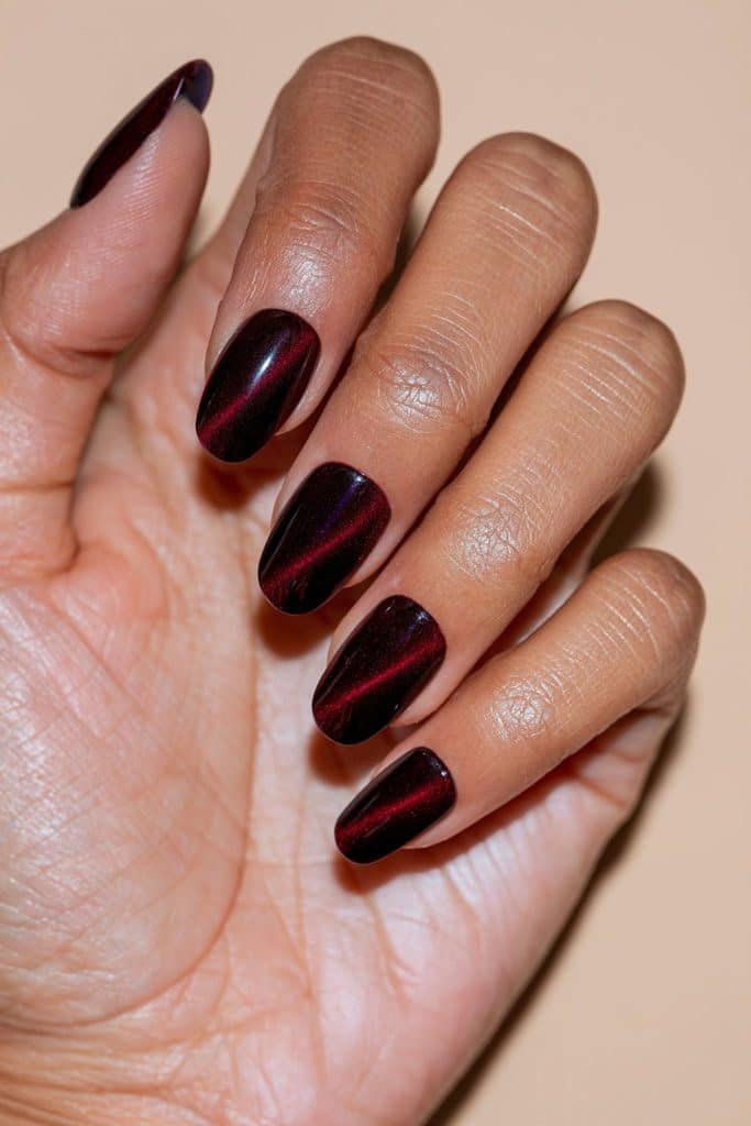 Maroon cat eye press-on nails featuring glossy burgundy polish, luminous ruby magnetic streaks, and an elegant oval shape.