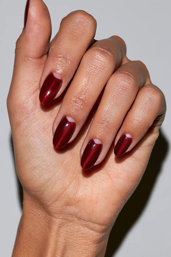 Red cat eye half-moon nails with glowing ruby magnetic crescents near the cuticles and a glossy cherry-red finish.