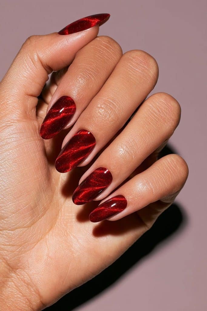 Red cat eye swirl nails with flowing ruby magnetic waves, luminous shimmer, and a glossy cherry-red finish.