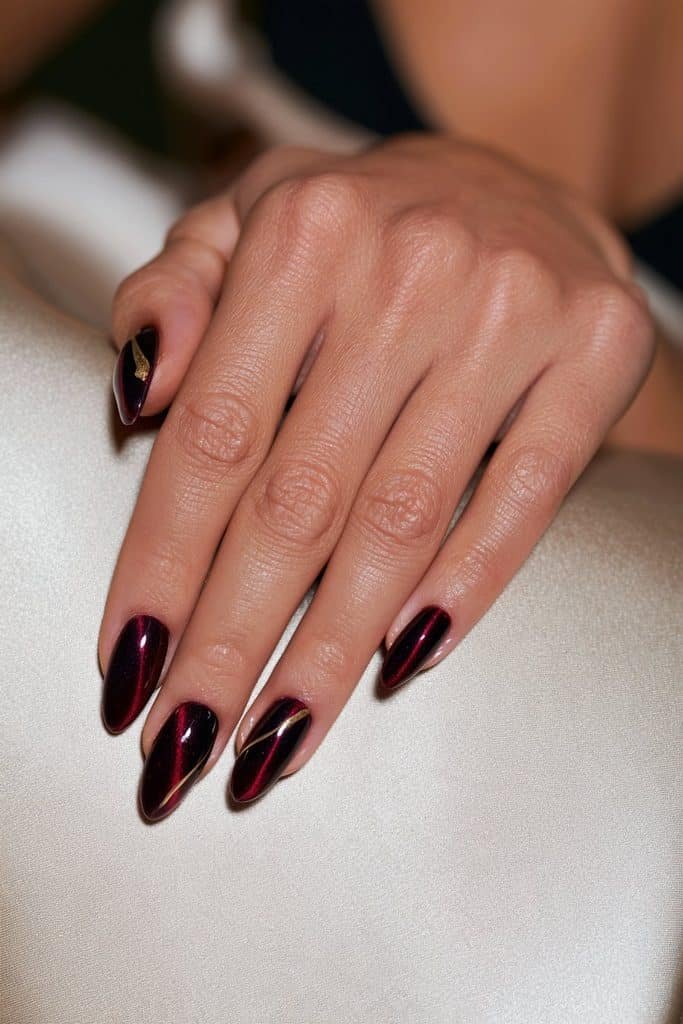 Plum-red cat eye nails with luminous magnetic shimmer, delicate gold lines, and subtle gold foil accents.