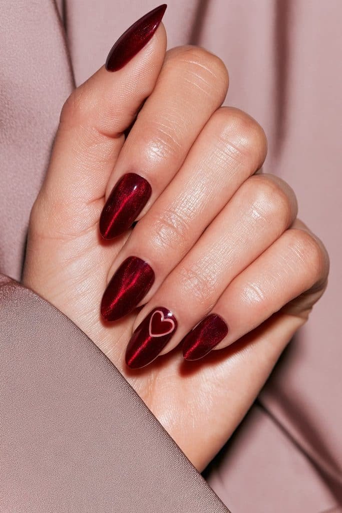 Cherry red cat eye nails with glowing ruby magnetic shimmer and a delicate heart accent on one nail.