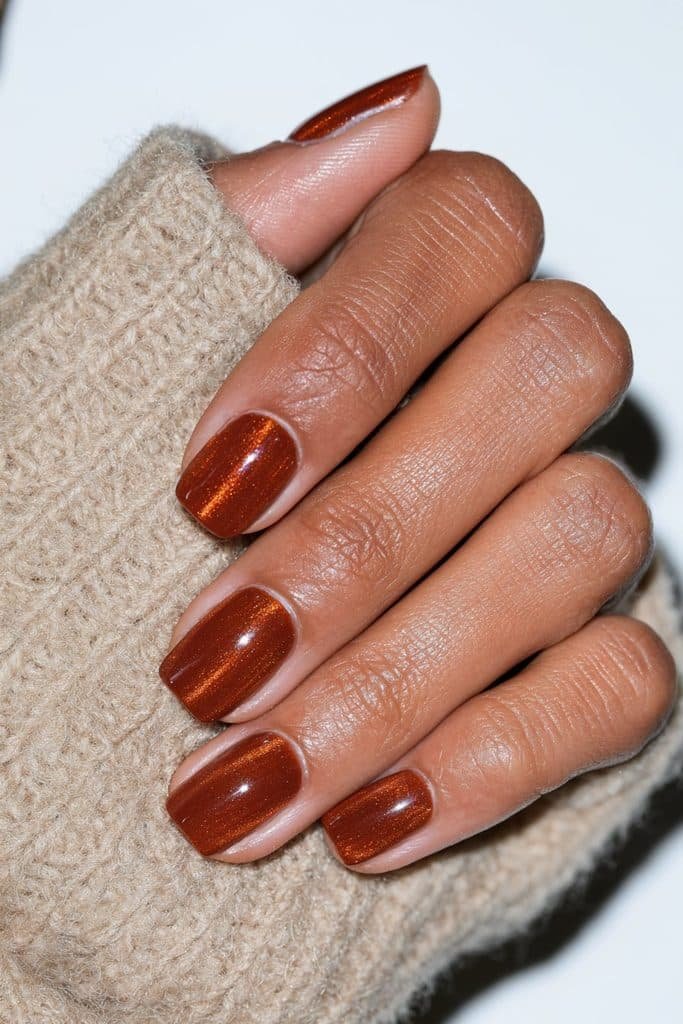 Short natural nails finished with glowing orange cat eye polish.