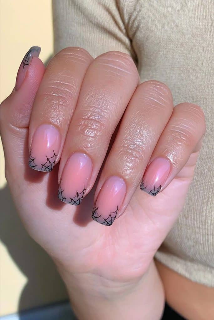 Short spider web nails with a sheer pink base and delicate black web accents