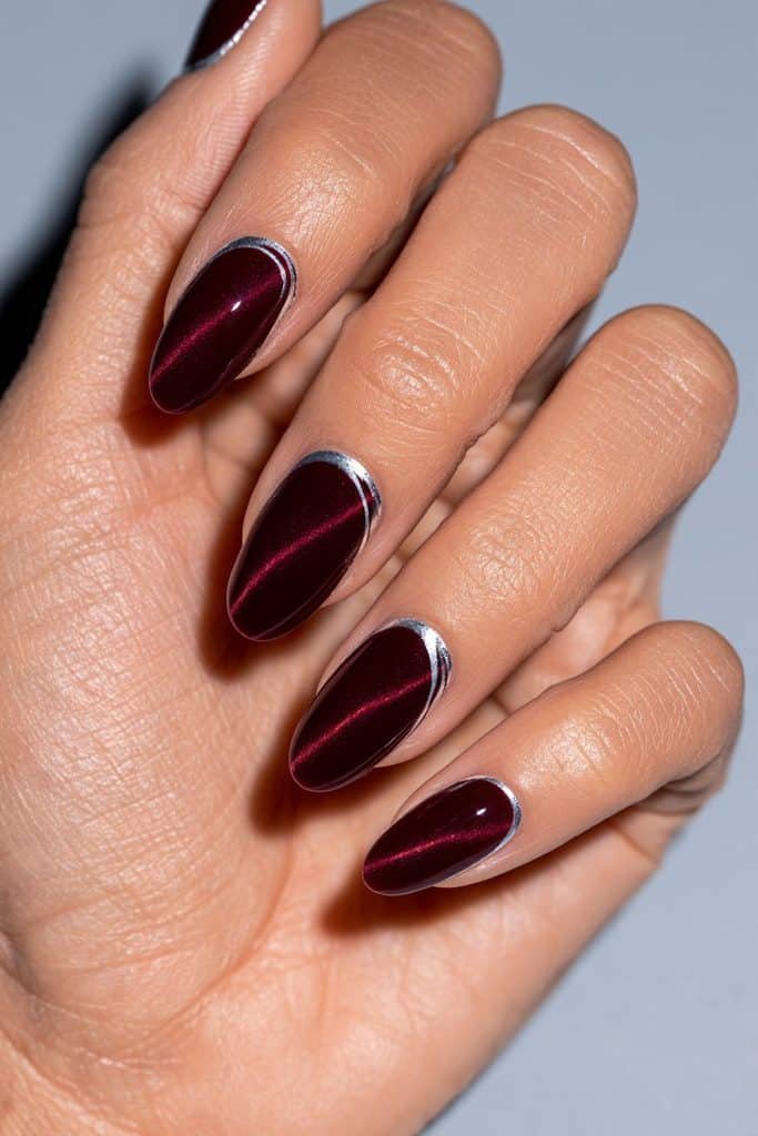 Maroon cat eye nails with thin silver chrome outlines, ruby magnetic streaks, and a glossy burgundy finish.