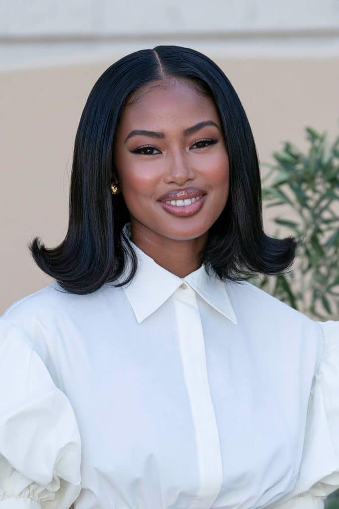 Black woman with a sleek flipped bob and middle part, featuring glossy, straight black hair with symmetrical ends flipped outward.