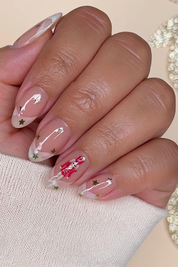 Minimalist nude nutcracker nails with one tiny red soldier accent and delicate gold stars