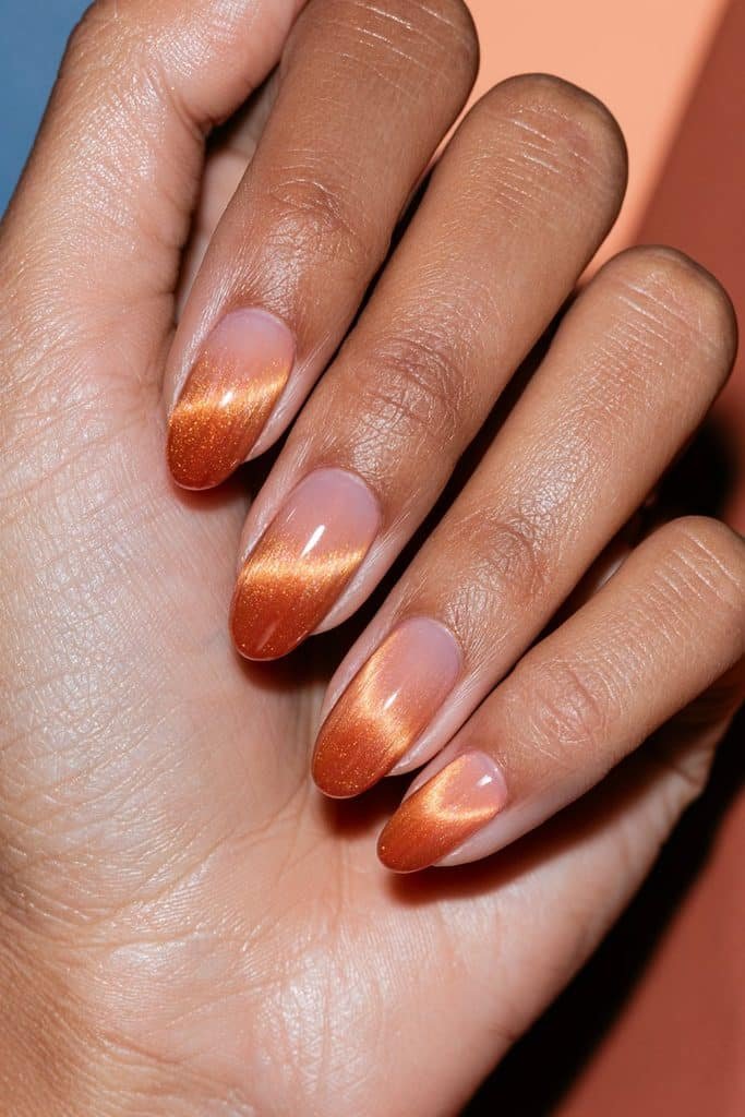 Burnt orange cat eye nails fading from deep orange at the cuticle to soft peach at the tips.