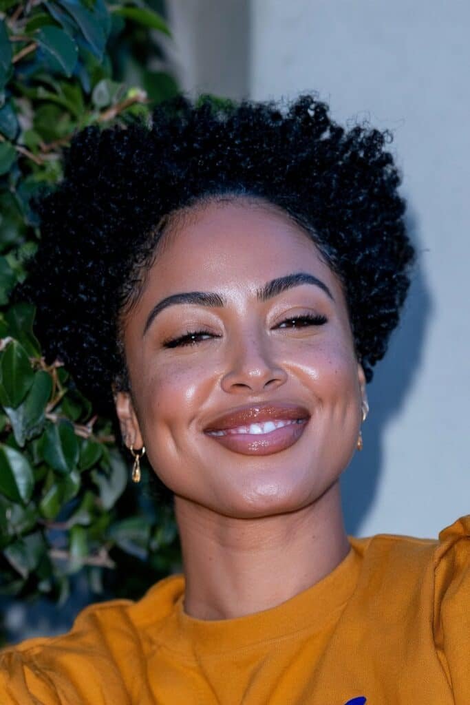 Black woman wearing a tapered afro haircut with voluminous natural curls on top and gradually faded sides.