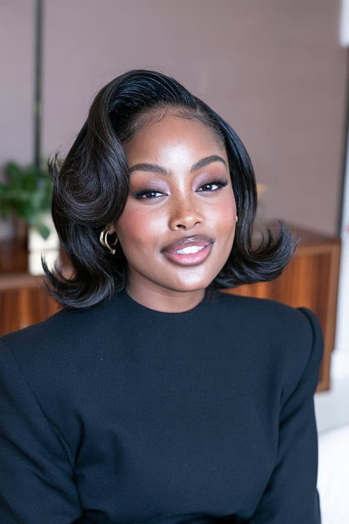 Black woman wearing a retro flip-flop bob with a dramatic swooping front section and outward-curled ends, inspired by vintage hairstyles.