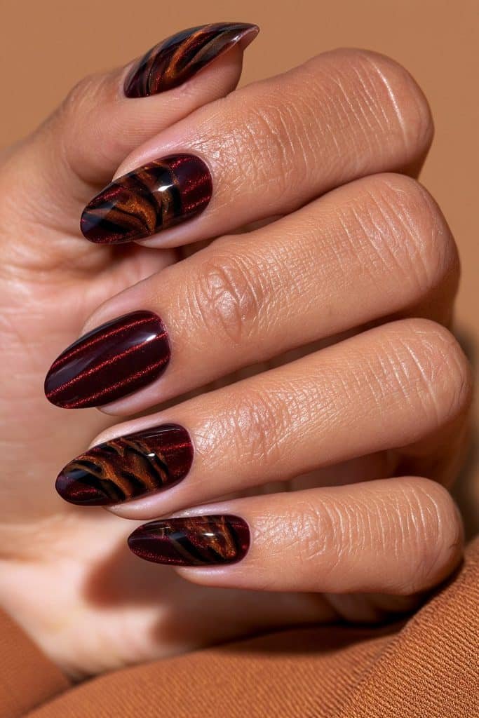 Maroon cat eye nails featuring caramel and espresso tortoiseshell swirls over a deep burgundy magnetic base.
