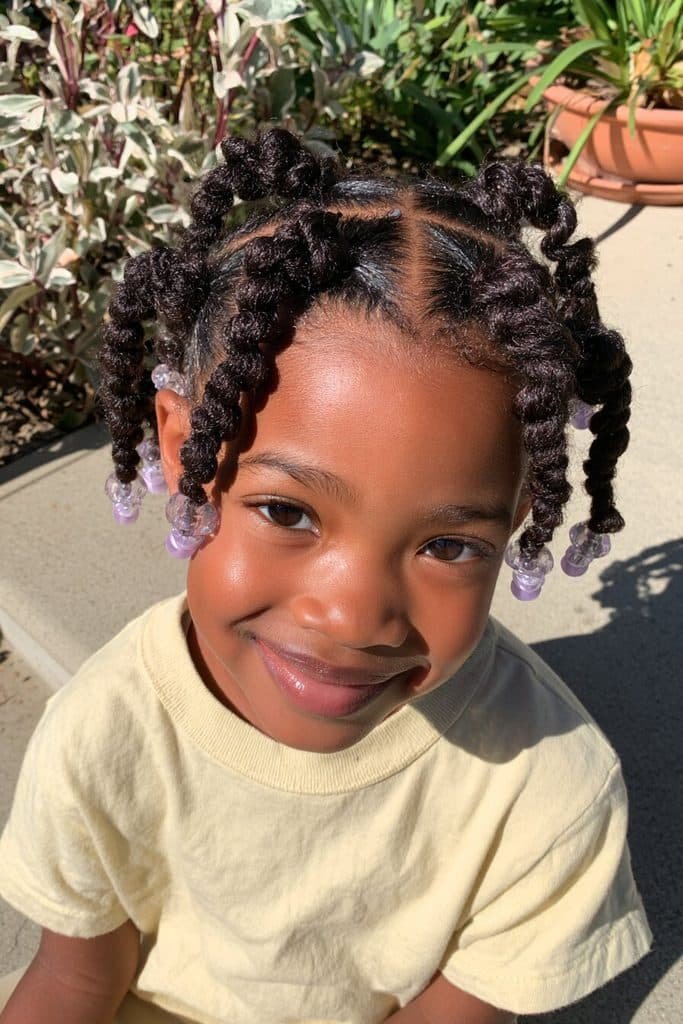Kids two-strand twists with neatly parted sections, defined natural texture, and clear and lavender beads.